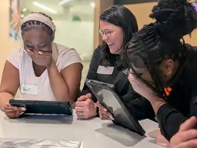 An adult volunteer and two students laugh at their life scenarios on tablets at Finance Park.